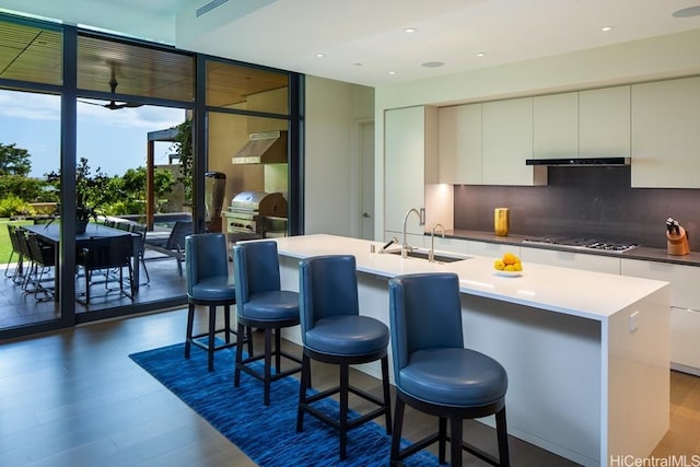 kitchen featuring decorative backsplash, dark wood-type flooring, sink, a center island with sink, and stainless steel gas stovetop