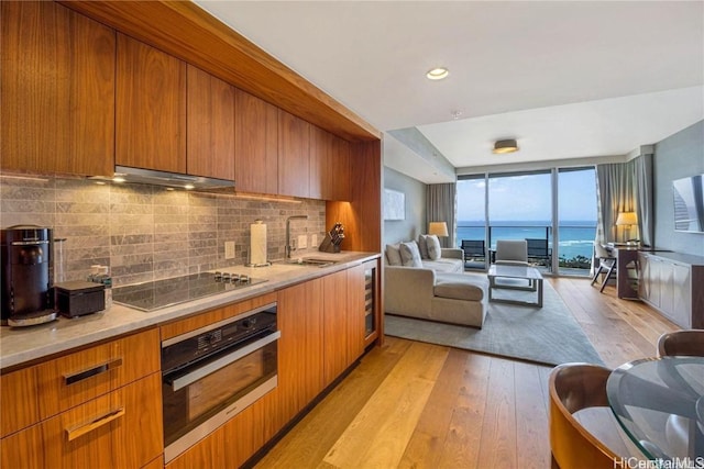 kitchen with stainless steel oven, sink, light wood-type flooring, range hood, and tasteful backsplash