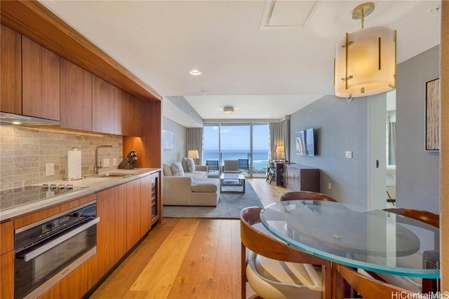 kitchen with sink, hanging light fixtures, oven, light hardwood / wood-style floors, and decorative backsplash