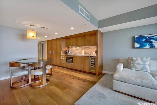 kitchen featuring decorative backsplash, stainless steel oven, light hardwood / wood-style flooring, wine cooler, and hanging light fixtures