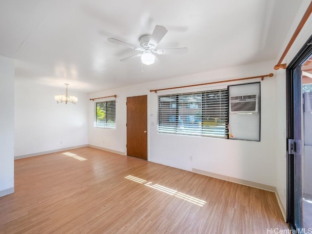 spare room with ceiling fan with notable chandelier, a wall mounted AC, and light hardwood / wood-style flooring