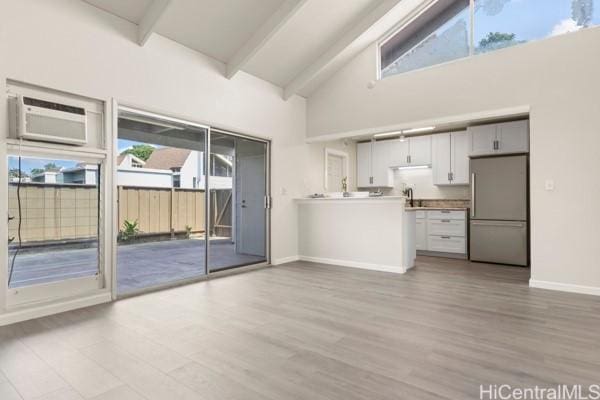 unfurnished living room featuring high vaulted ceiling, plenty of natural light, light wood-type flooring, and a wall unit AC