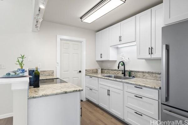 kitchen with white cabinets, stainless steel fridge, light stone countertops, and sink