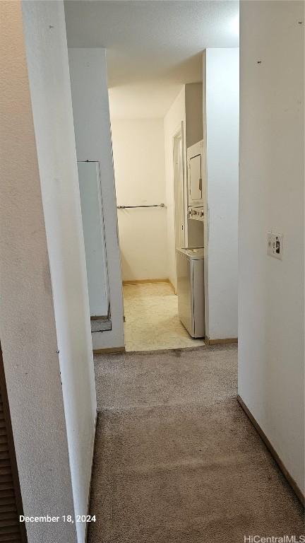 hall with light carpet and stacked washer and clothes dryer