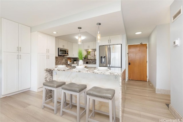 kitchen featuring white cabinetry, decorative light fixtures, light wood-type flooring, appliances with stainless steel finishes, and light stone countertops