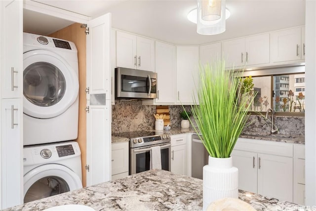 kitchen featuring sink, stainless steel appliances, stacked washer and clothes dryer, tasteful backsplash, and white cabinets