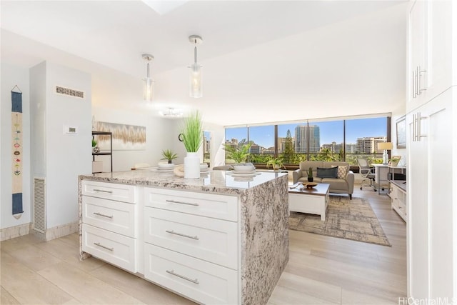 kitchen with light hardwood / wood-style flooring, white cabinetry, a center island, light stone counters, and decorative light fixtures