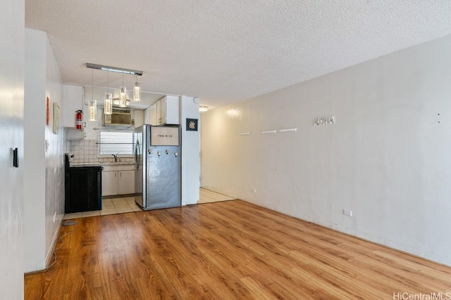 kitchen featuring stainless steel refrigerator, white cabinetry, electric range, decorative backsplash, and light wood-type flooring