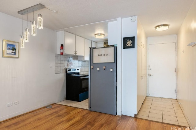 kitchen with pendant lighting, range with electric cooktop, decorative backsplash, stainless steel fridge, and white cabinetry