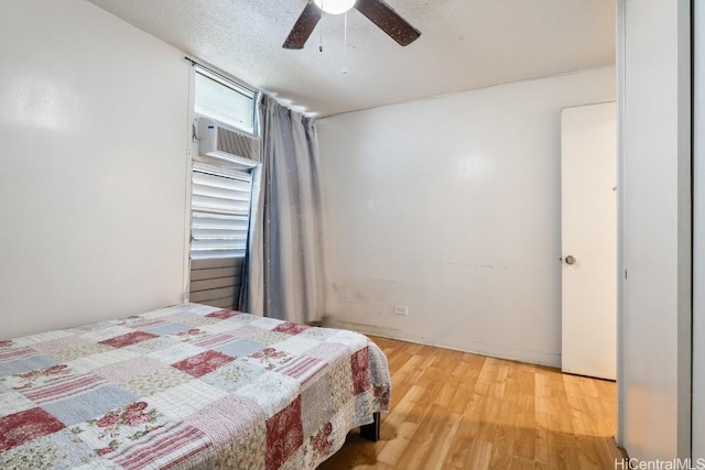 bedroom with ceiling fan, a textured ceiling, a wall mounted AC, and light hardwood / wood-style flooring