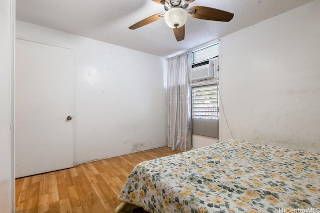 bedroom featuring a wall unit AC, ceiling fan, light hardwood / wood-style floors, and a textured ceiling