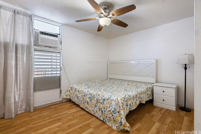 bedroom featuring ceiling fan, cooling unit, light wood-type flooring, and a textured ceiling