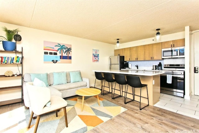 kitchen with a breakfast bar, a center island, light hardwood / wood-style floors, stainless steel appliances, and a textured ceiling