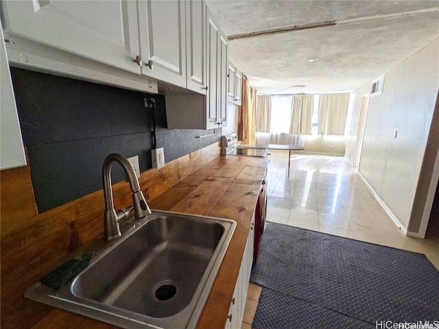 kitchen with white cabinets, light tile patterned floors, range, and sink