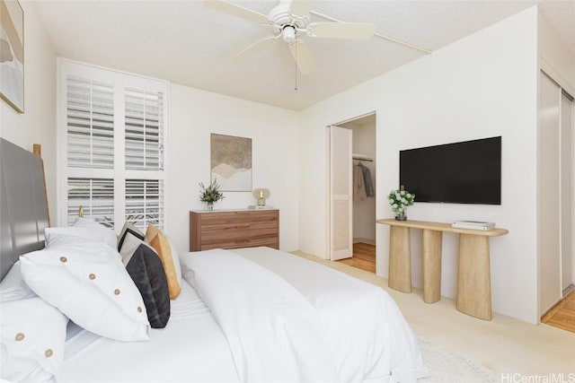 bedroom with a walk in closet, light colored carpet, a closet, and ceiling fan