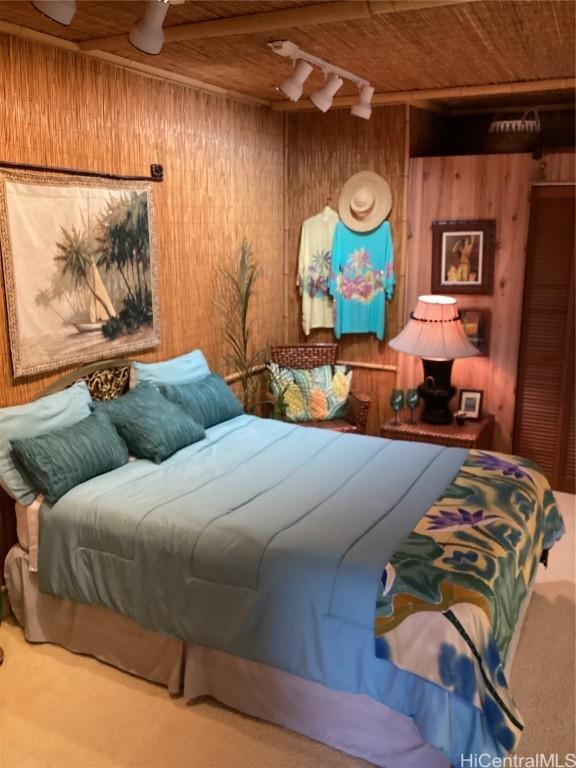 bedroom featuring beam ceiling, wooden ceiling, track lighting, and wooden walls