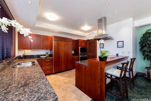 kitchen with island exhaust hood, a kitchen bar, stainless steel oven, built in microwave, and sink