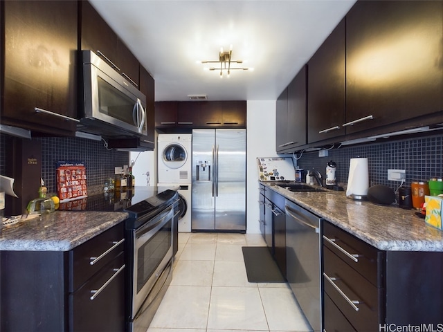 kitchen featuring tasteful backsplash, light tile patterned flooring, dark brown cabinetry, stacked washer / dryer, and stainless steel appliances