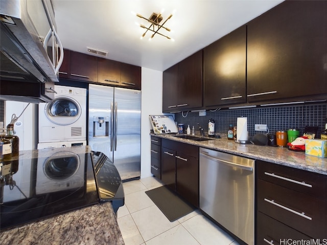 kitchen with sink, tasteful backsplash, stacked washer and dryer, dark brown cabinets, and appliances with stainless steel finishes