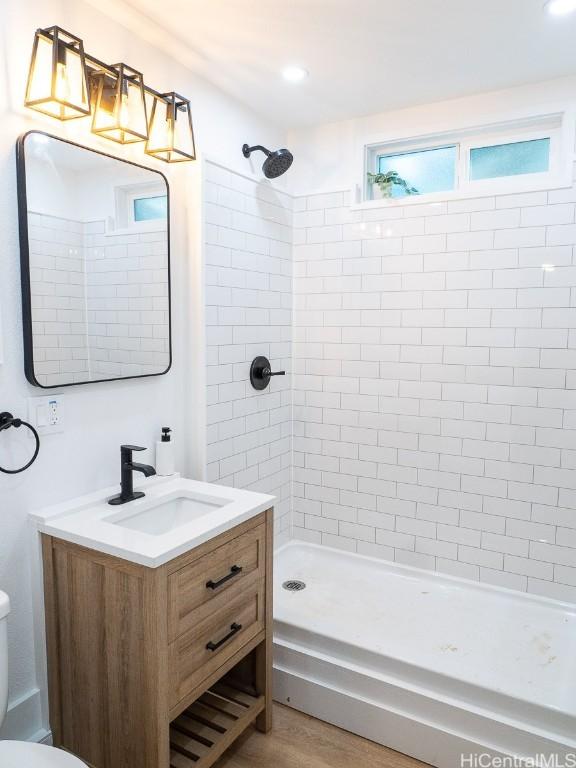 bathroom featuring a tile shower, hardwood / wood-style flooring, vanity, and toilet