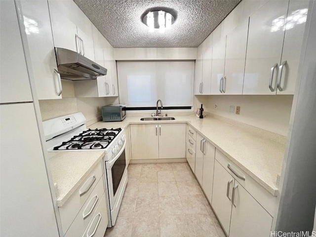 kitchen with a textured ceiling, light tile patterned flooring, under cabinet range hood, white appliances, and a sink