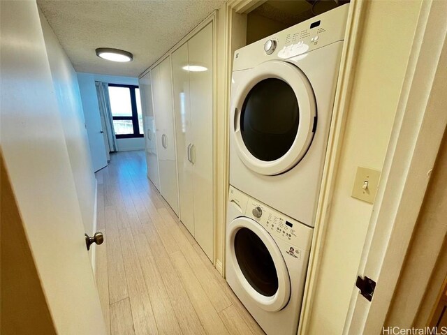 washroom with light wood-type flooring, stacked washing maching and dryer, and a textured ceiling