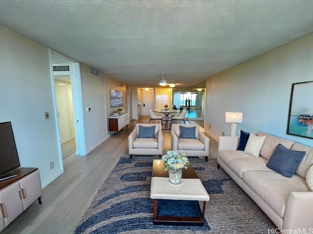 living room featuring ceiling fan, light hardwood / wood-style flooring, and a textured ceiling