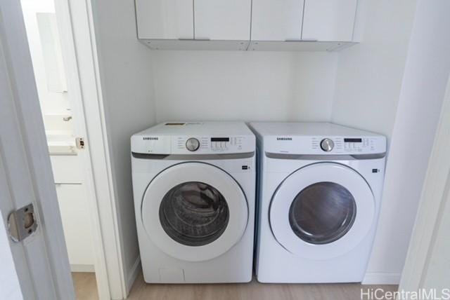 clothes washing area with cabinets, separate washer and dryer, and light hardwood / wood-style floors