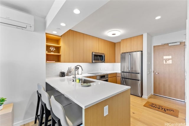 kitchen with an AC wall unit, sink, light hardwood / wood-style floors, kitchen peninsula, and stainless steel appliances