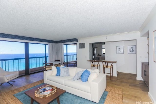 living room featuring crown molding, a water view, wood-type flooring, and a textured ceiling