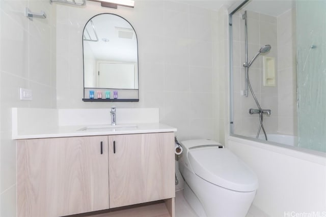 full bathroom with vanity, toilet, bath / shower combo with glass door, and tile walls