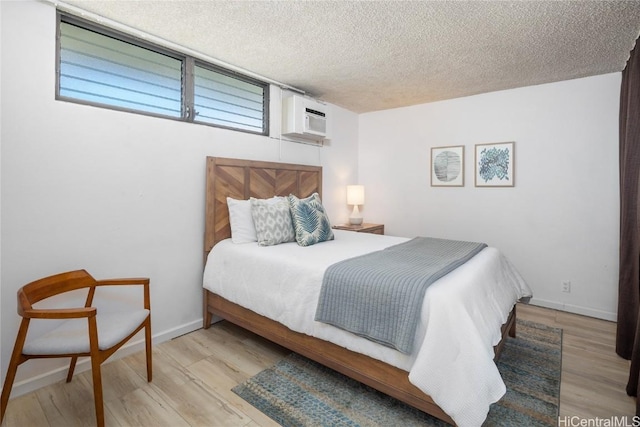 bedroom with an AC wall unit, a textured ceiling, and light hardwood / wood-style flooring