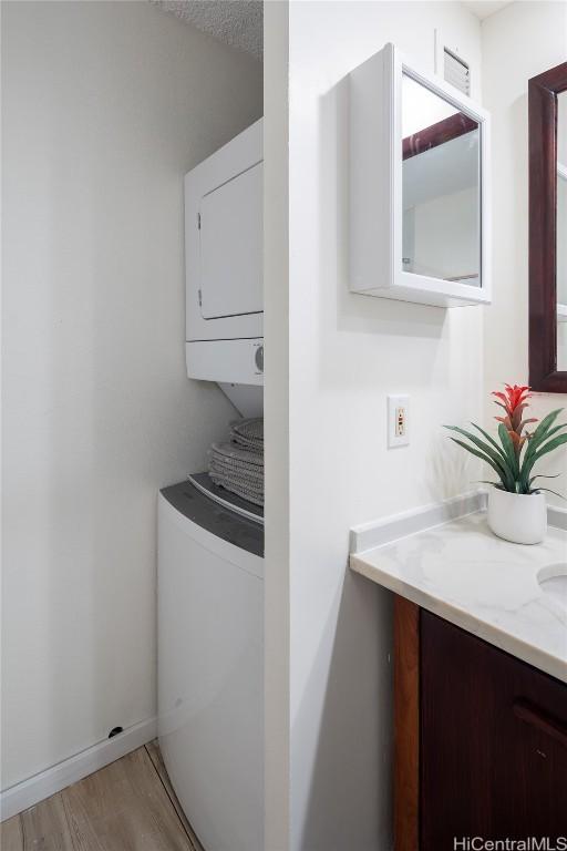 clothes washing area featuring stacked washer / dryer, light hardwood / wood-style flooring, and a textured ceiling