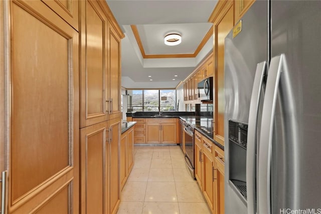 kitchen featuring a tray ceiling, light tile patterned floors, dark countertops, appliances with stainless steel finishes, and ornamental molding