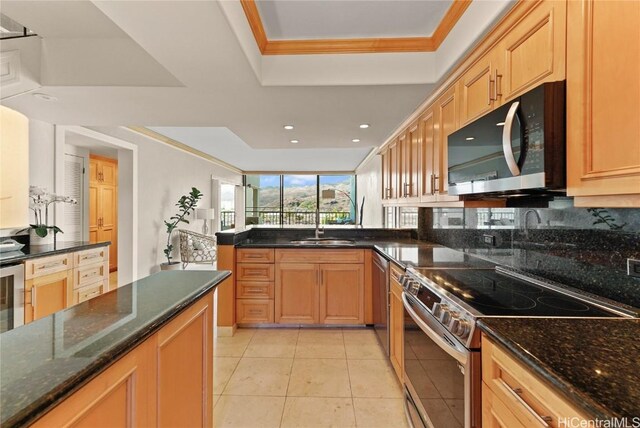 kitchen with sink, stainless steel appliances, a raised ceiling, dark stone countertops, and light tile patterned flooring