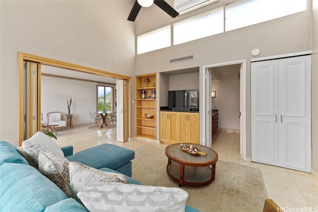 tiled living room featuring built in shelves, ceiling fan, and a towering ceiling