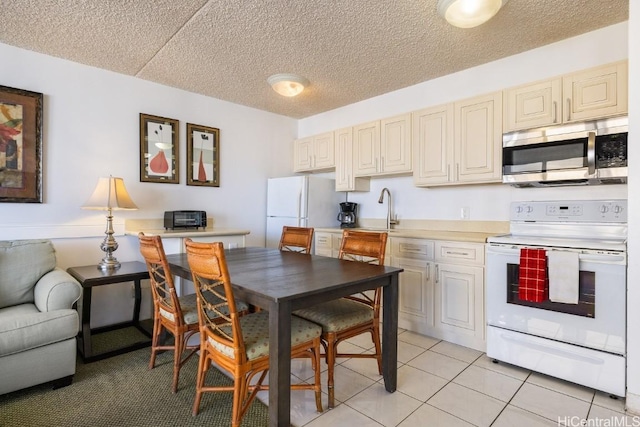 kitchen featuring cream cabinetry, white appliances, sink, and light tile patterned floors