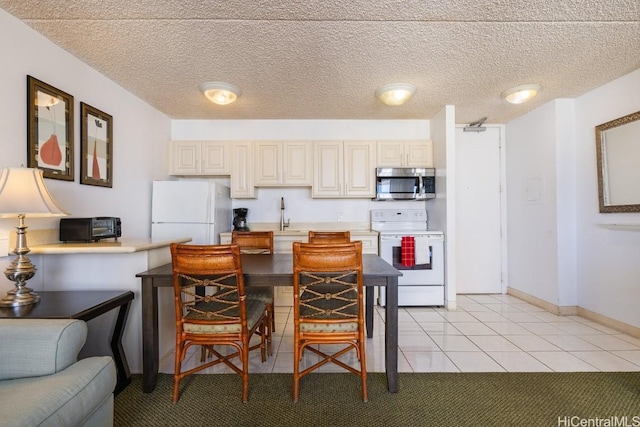 kitchen featuring cream cabinetry, white appliances, a textured ceiling, and light tile patterned floors