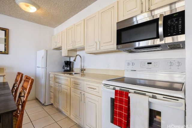 kitchen featuring a textured ceiling, white appliances, sink, light tile patterned floors, and cream cabinets