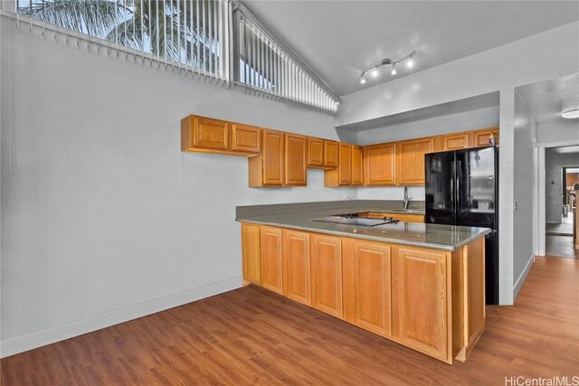 kitchen featuring a high ceiling, cooktop, light hardwood / wood-style flooring, kitchen peninsula, and black refrigerator