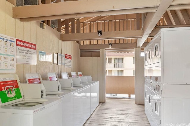 clothes washing area with washing machine and clothes dryer, wooden walls, stacked washing maching and dryer, and light hardwood / wood-style floors