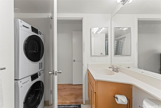 washroom with sink, hardwood / wood-style floors, and stacked washer and clothes dryer