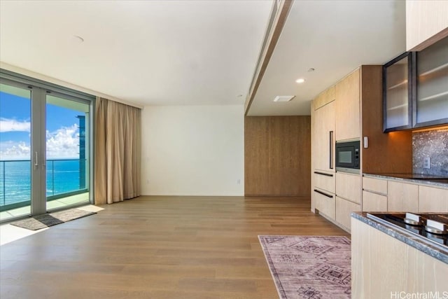 kitchen with floor to ceiling windows, a water view, light brown cabinetry, light hardwood / wood-style floors, and black microwave