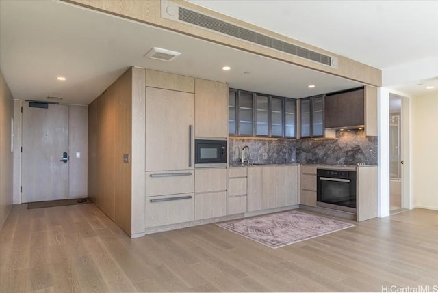 kitchen featuring black microwave, light brown cabinetry, oven, and light hardwood / wood-style floors