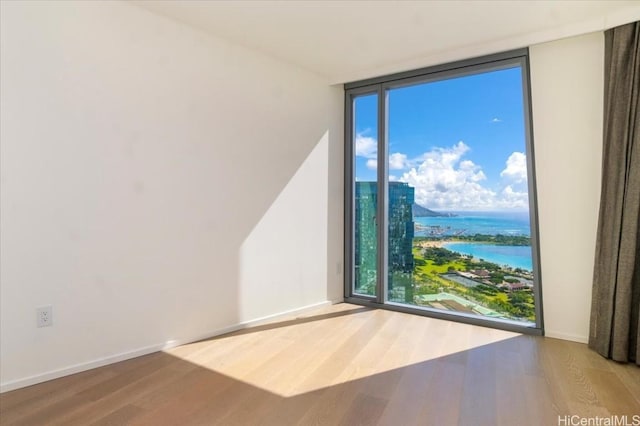 empty room featuring hardwood / wood-style floors, a water view, and a wall of windows