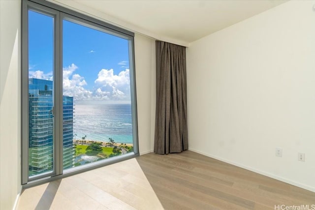 unfurnished room with floor to ceiling windows, a water view, and light hardwood / wood-style floors