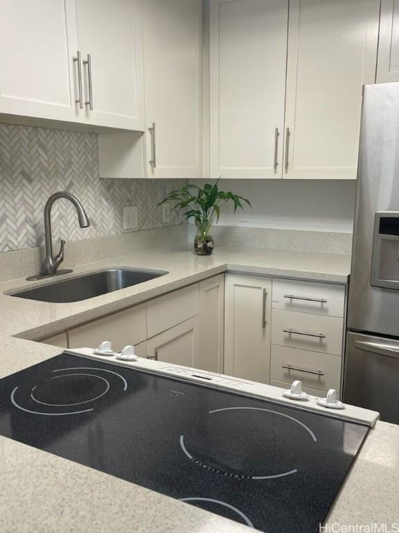 kitchen with white cabinetry, backsplash, stainless steel fridge, and sink