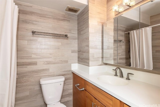 bathroom featuring vanity, toilet, tile walls, and walk in shower