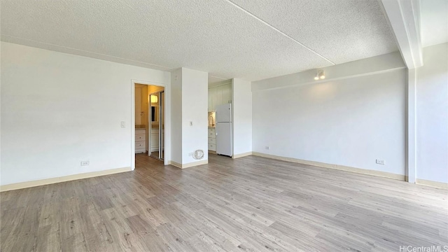 spare room featuring beamed ceiling, a textured ceiling, and light hardwood / wood-style floors