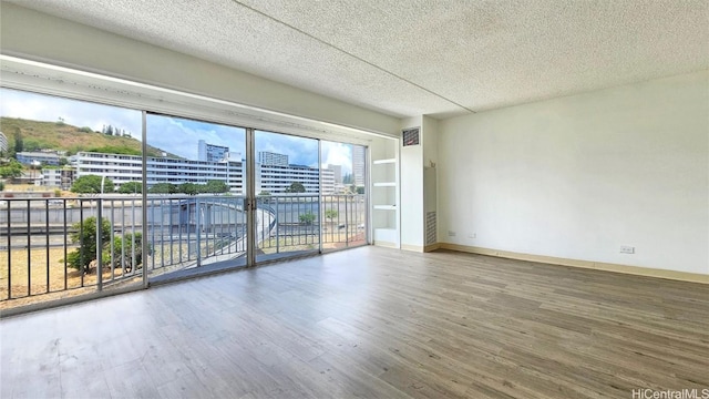 empty room with wood-type flooring, a textured ceiling, and built in shelves